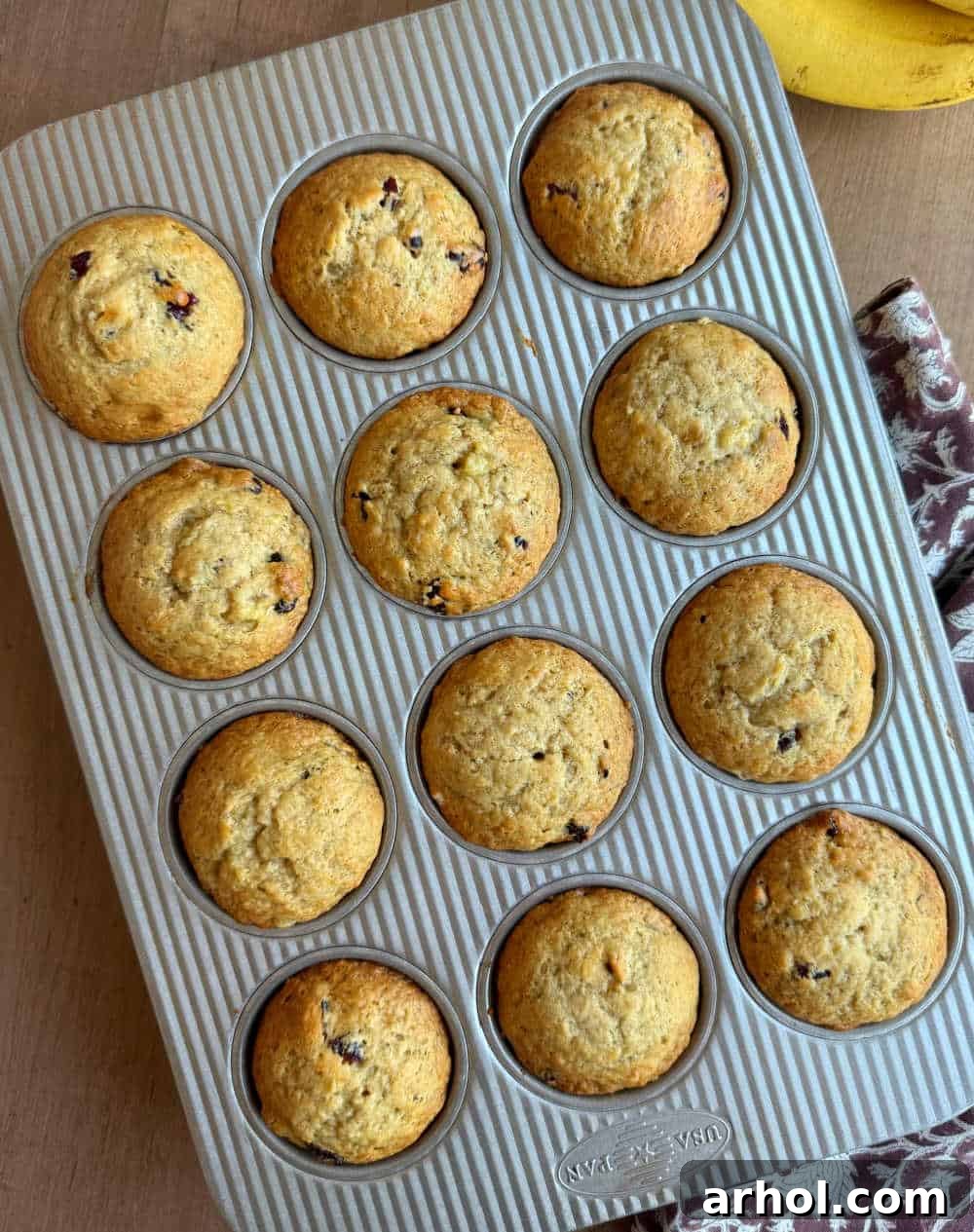 Sweet and Tart Banana Cranberry Muffins 7 Freshly baked banana cranberry muffins, perfectly risen and golden, cooling in a non-stick muffin tin after being removed from the oven.