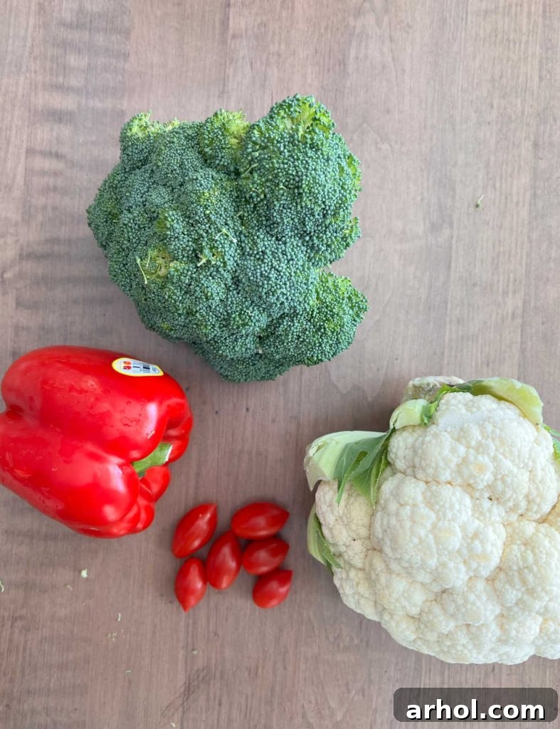 Prepped broccoli florets, bell pepper strips, grape tomatoes, and cauliflower florets arranged on a cutting board, ready for assembly.