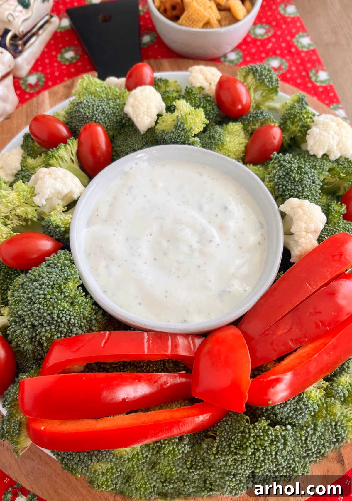 Finished Christmas veggie wreath platter with raw broccoli, cauliflower, tomatoes, and a red bell pepper bow, ready to serve on a rustic wooden table.