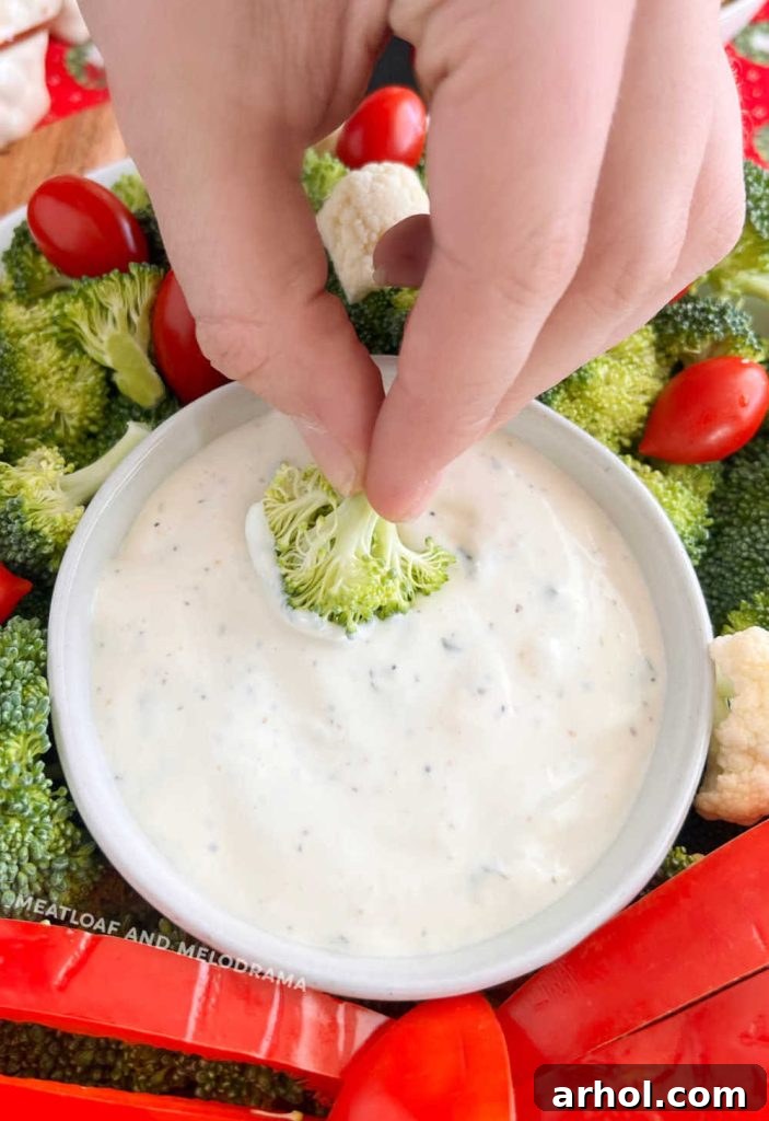 Hand dipping a fresh raw broccoli floret into a bowl of creamy ranch dressing, highlighting the delicious pairing.
