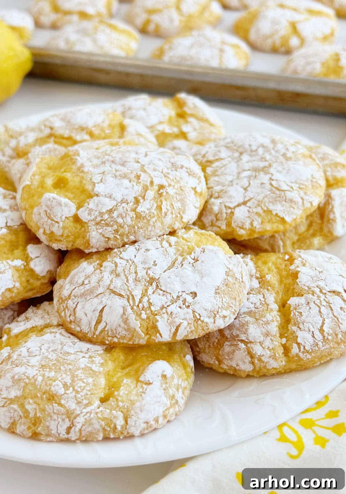 A white plate showcasing several easy lemon cake mix crinkle cookies, each beautifully coated in powdered sugar with visible cracks.