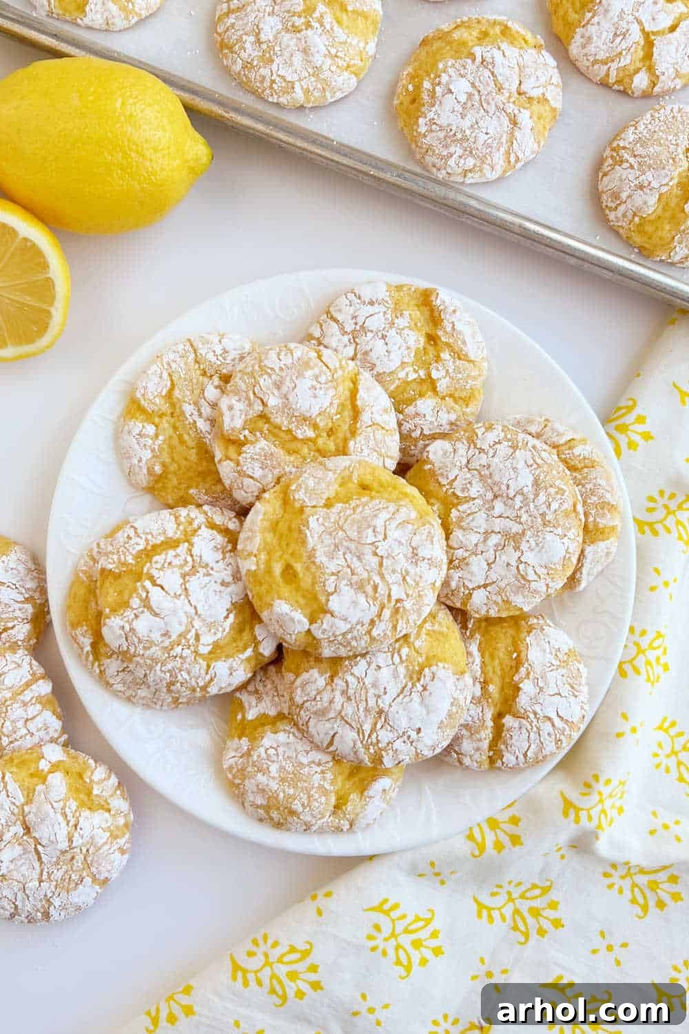 A pristine white plate generously filled with freshly baked lemon cake mix cookies, artfully dusted with powdered sugar, sitting on a rustic wooden table, ready to be enjoyed.