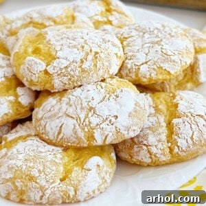A stack of golden lemon crinkle cookies, generously coated with powdered sugar, resting on a white plate, highlighting their soft texture.