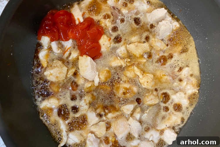 Chicken browning in a frying pan with a bowl of bourbon sauce ingredients nearby.