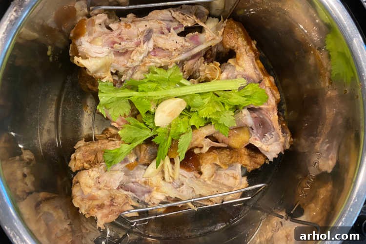 Rotisserie chicken carcass, celery leaves, and whole garlic cloves placed on a trivet inside an Instant Pot liner, ready for broth making.