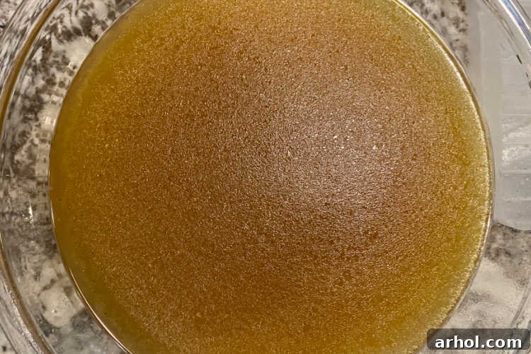 A large bowl filled with rich, golden homemade chicken stock, ready for straining and use in the soup.