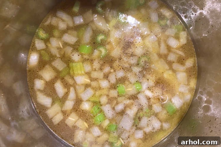Instant Pot filled with rich chicken broth, sautéed onions, and celery, with orzo pasta added, ready for the final pressure cooking stage.