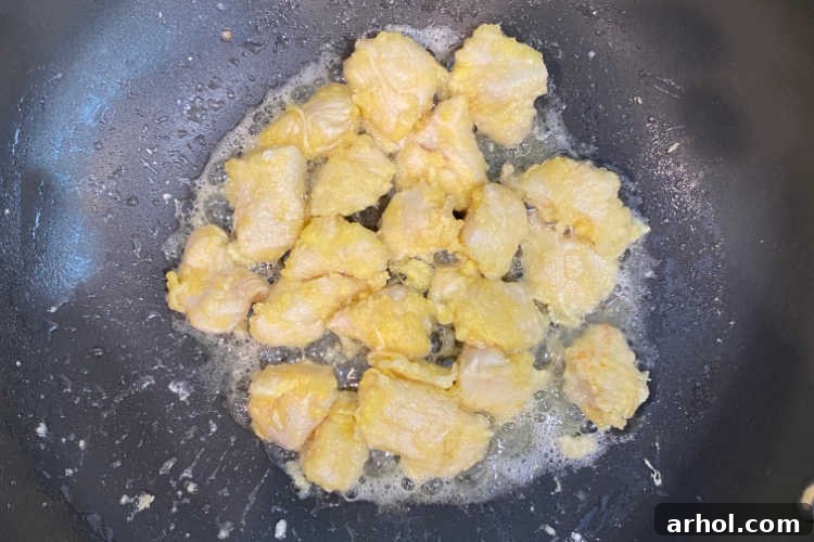 Effortless Zesty Orange Chicken 5 Golden brown cubed chicken pieces cooking in a wok over medium-high heat, showing the progress of frying for crispy texture