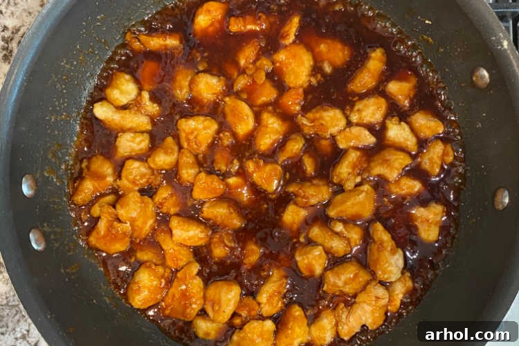 Effortless Zesty Orange Chicken 7 Crispy orange chicken pieces simmering in the vibrant orange marmalade and BBQ sauce on the stove, getting coated and thickened