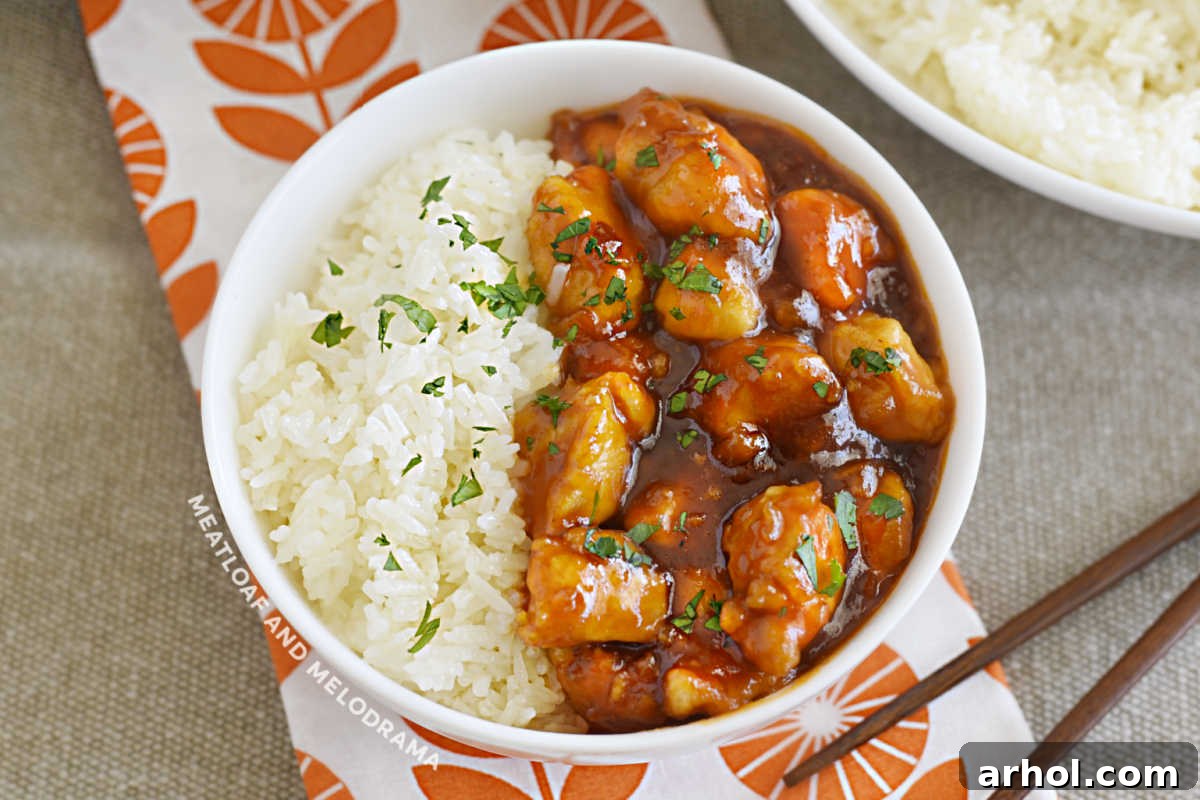 Effortless Zesty Orange Chicken 8 Delicious orange chicken with marmalade and BBQ sauce in a white bowl, served over a bed of fluffy rice, garnished with sesame seeds and green onions