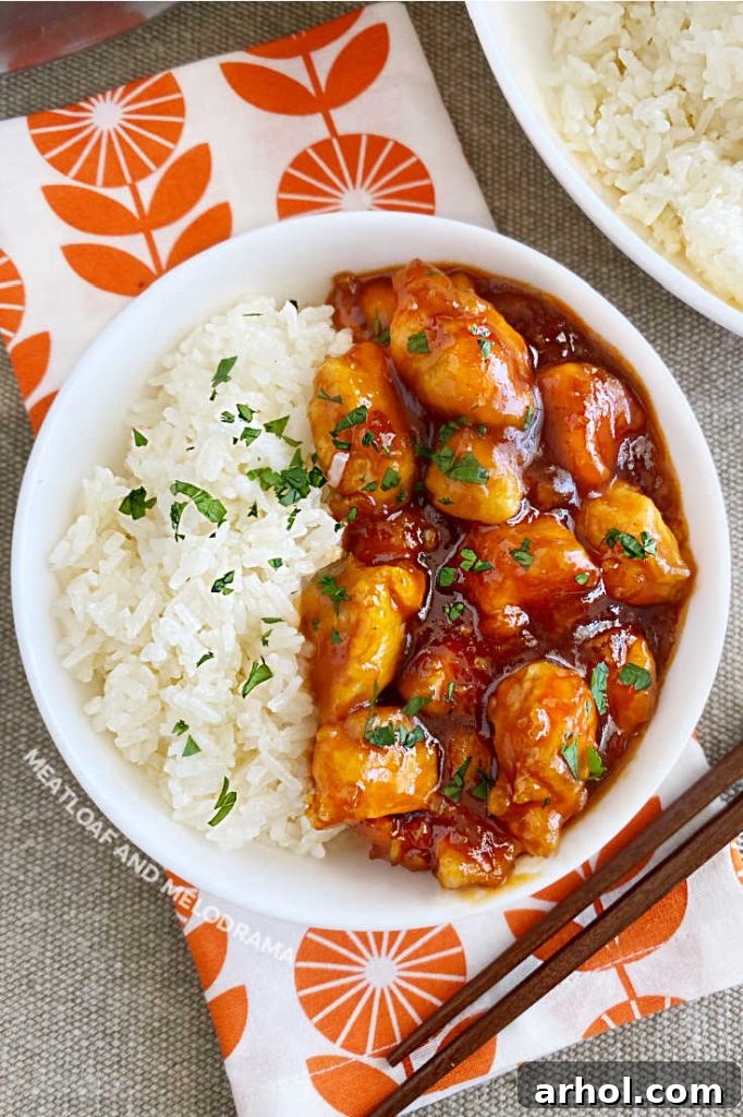 Effortless Zesty Orange Chicken 9 A bowl of homemade orange chicken pieces and rice on a dining table, garnished with green onions, ready to be enjoyed