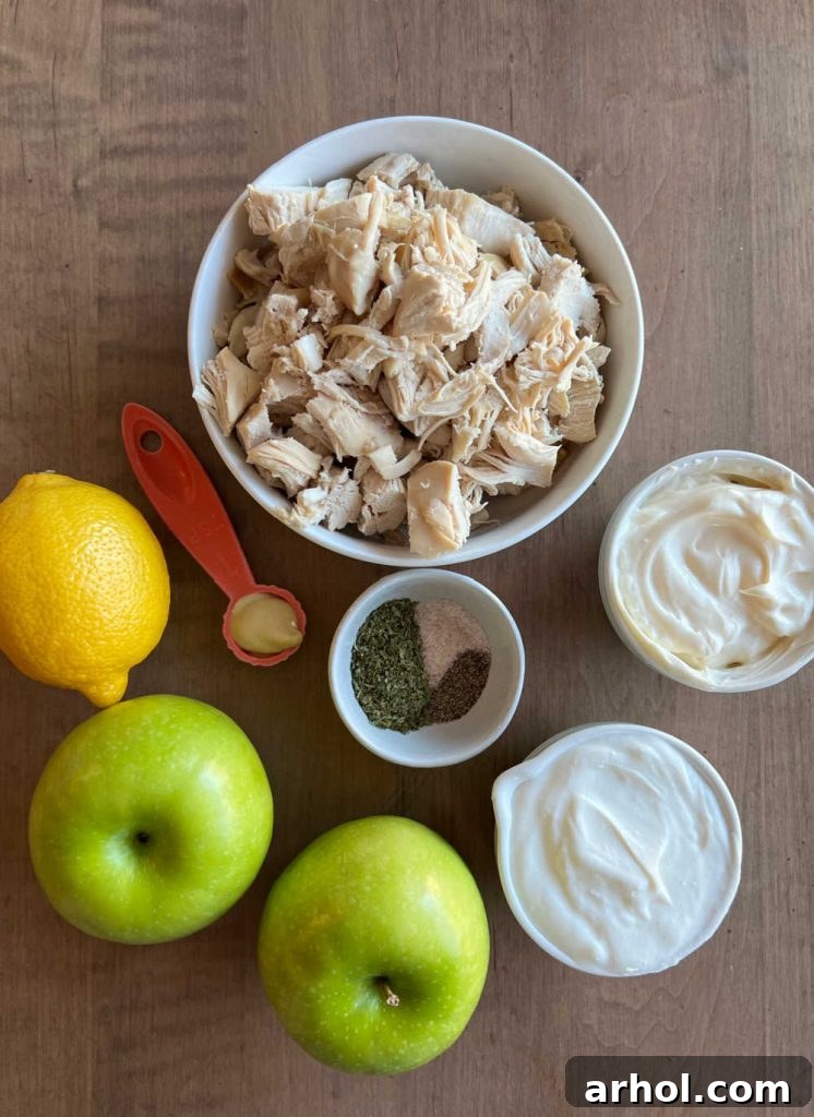 An array of fresh ingredients for lemon chicken salad, including leftover cooked chicken, creamy mayonnaise, Greek yogurt, crisp apples, bright lemons, tangy Dijon mustard, and various seasonings, laid out on a rustic wooden surface.