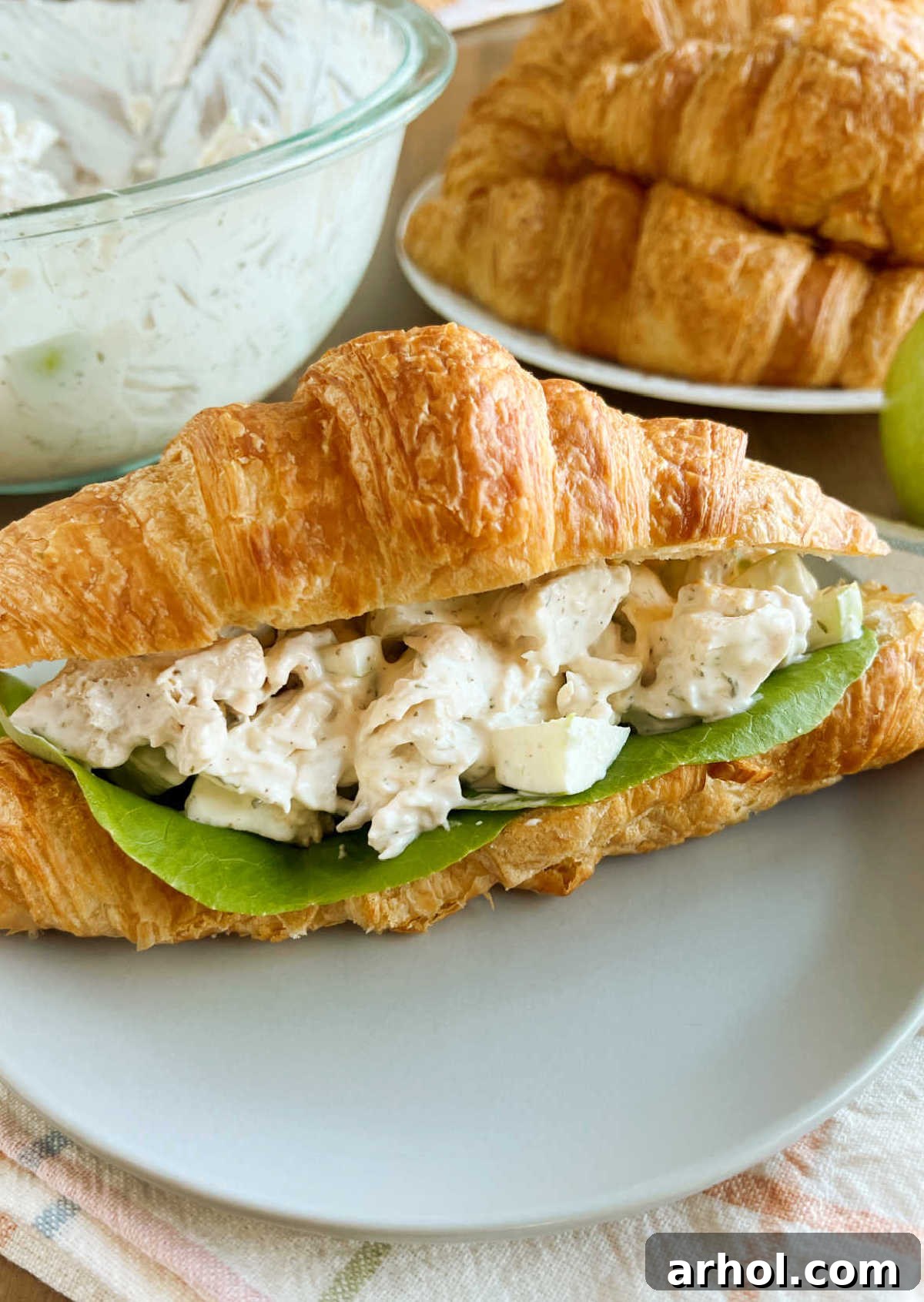 Lemon chicken salad, rich and creamy, generously stuffed into a fluffy croissant roll, artfully presented to highlight its enticing texture and vibrant colors.