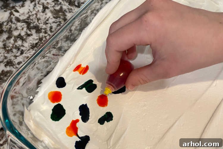 Dropping vibrant food coloring onto a layer of white Cool Whip in a baking dish, ready for swirling.