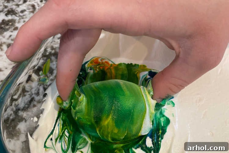 A hard-boiled egg being gently rolled in a vibrant mixture of Cool Whip and food coloring to achieve a marbled effect.
