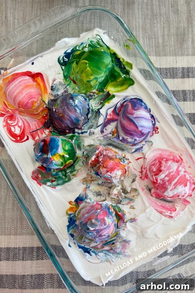 Several hard-boiled eggs resting in a baking dish, fully covered in colorful Cool Whip and food coloring mixture.