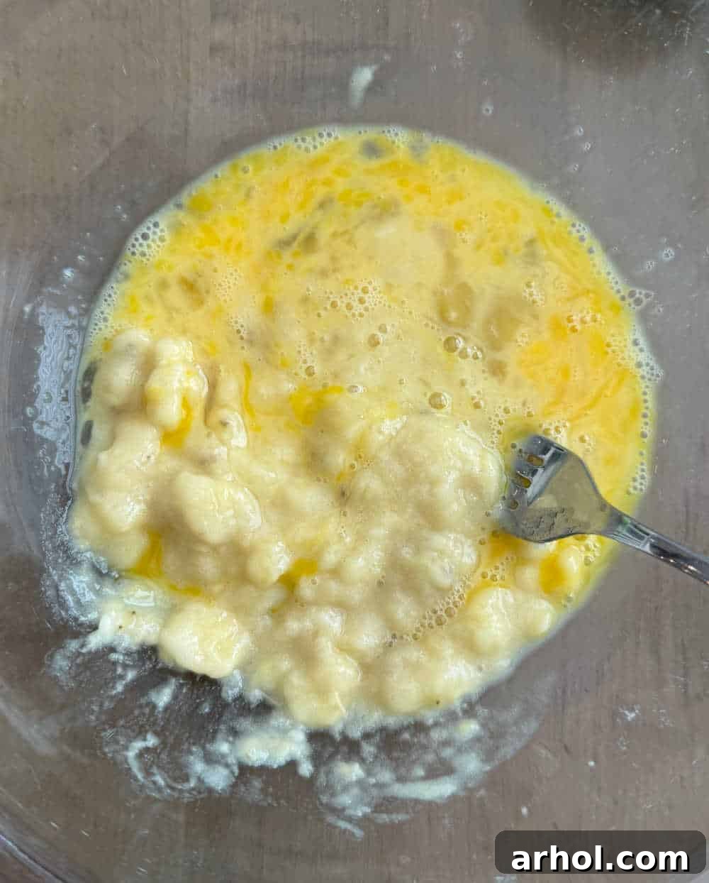 Step-by-step image showing ripe bananas being mashed with eggs in a mixing bowl.