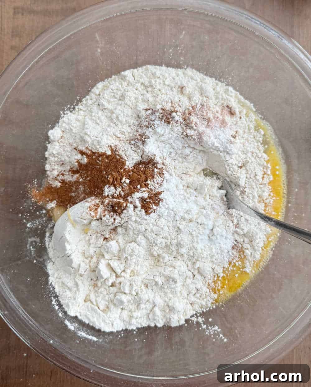 Dry ingredients, including flour and sugar, being added to the bowl with mashed bananas and eggs.