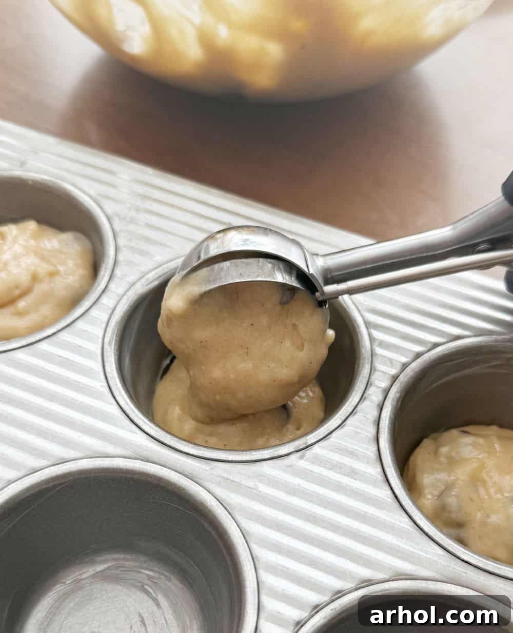 Banana bread muffin batter being scooped into a greased muffin tin, ready for baking.