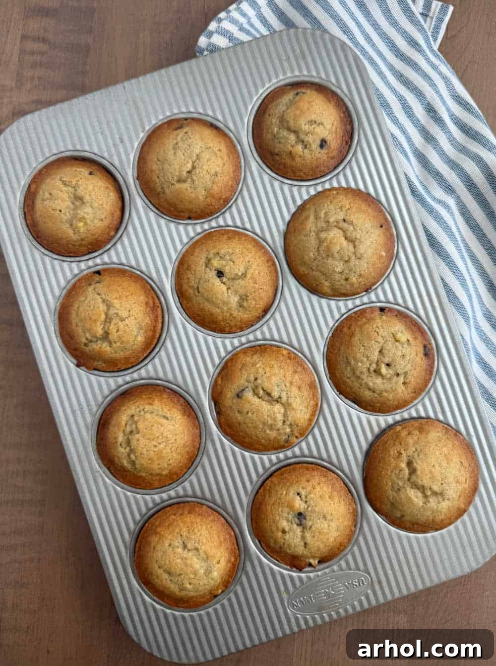 Freshly baked golden brown banana bread muffins cooling in a muffin pan.