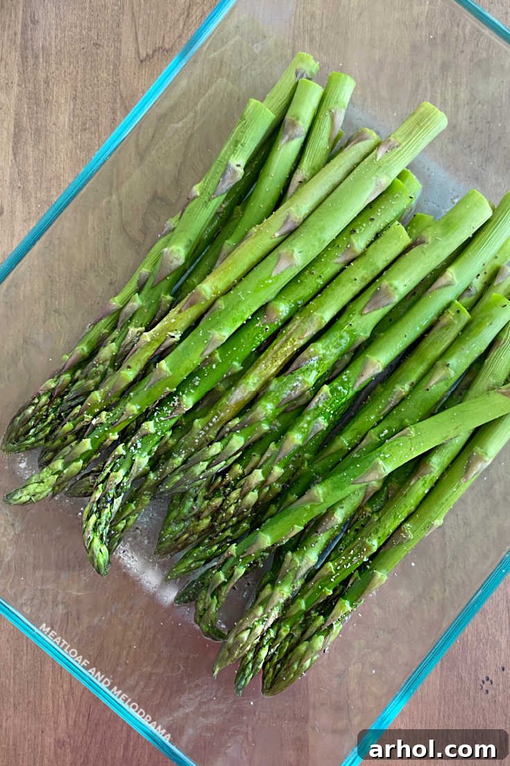 fresh asparagus with water, salt, pepper and garlic powder in glass dish