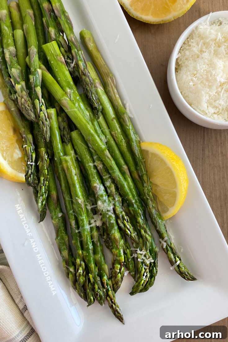 microwave asparagus on a white platter with lemon slices and parmesan cheese