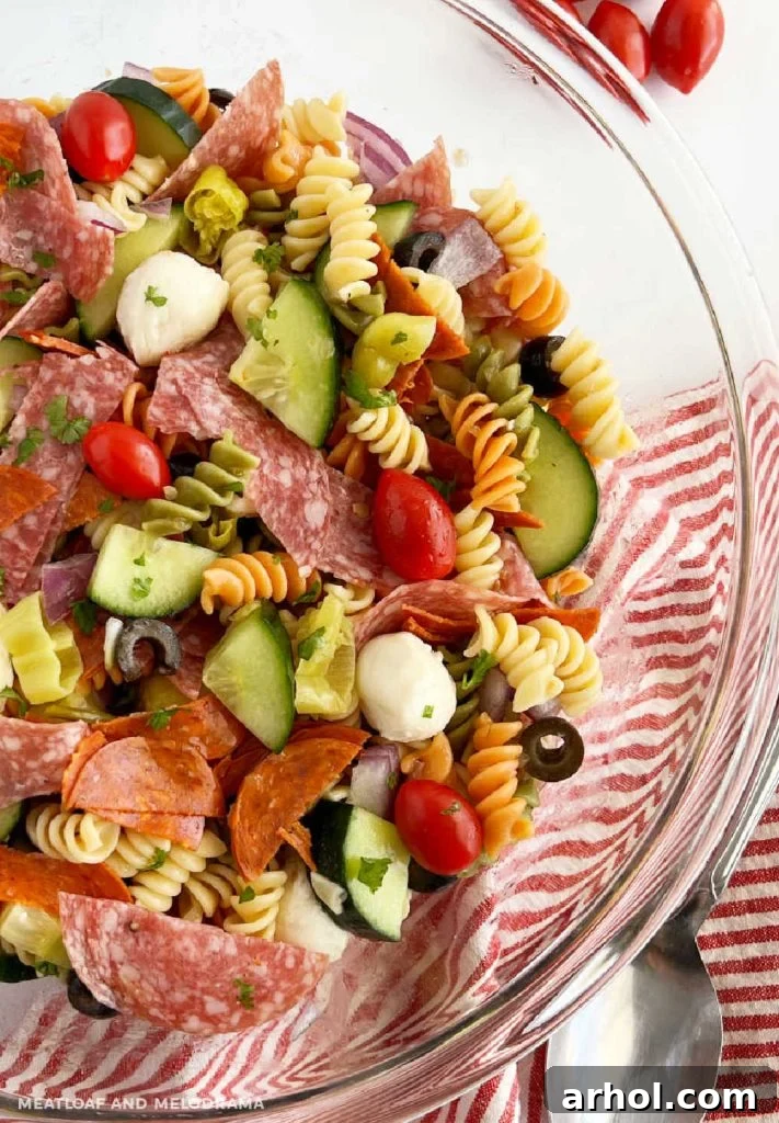 Vibrant Italian pasta salad with pepperoni, salami, rotini pasta, and fresh vegetables in a large serving bowl, garnished with fresh herbs.