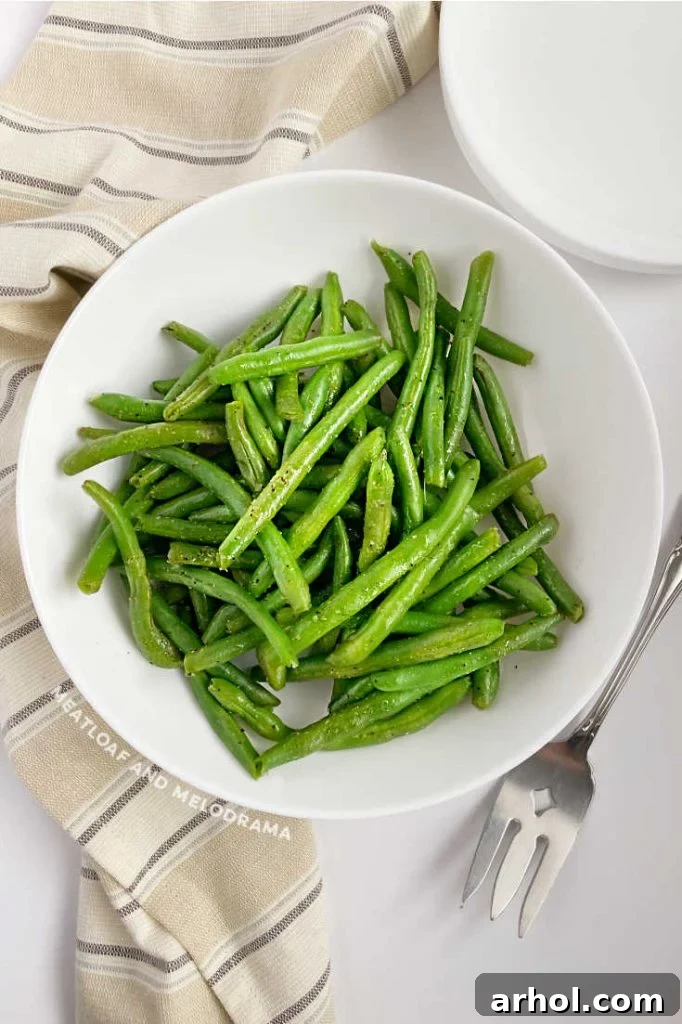 Steamed green beans in a pristine white serving dish, ready to be enjoyed with a fork