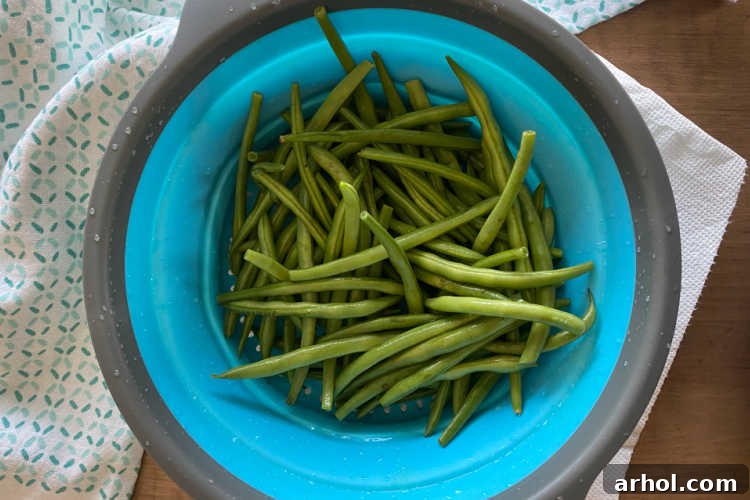 Fresh green beans glistening with water in a blue colander