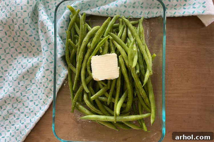Fresh green beans in a glass dish with a pat of butter and seasonings