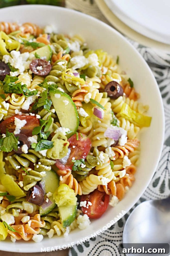 Close-up of vibrant Greek pasta salad featuring tri-color rotini, juicy tomatoes, olives, feta, and cucumber, showcasing the fresh texture.