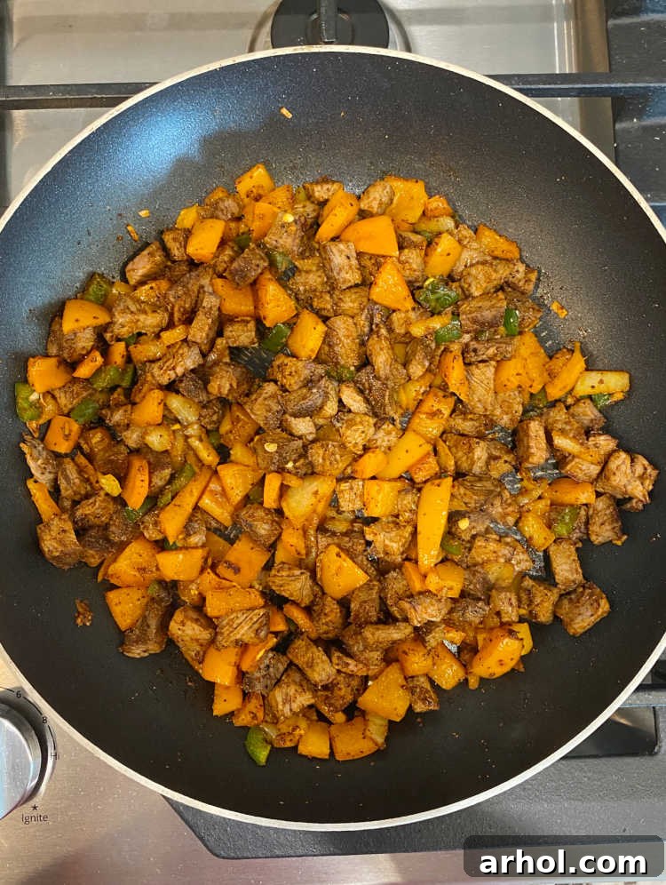 Seasoned steak, bell peppers, and onion mixture cooking in a skillet