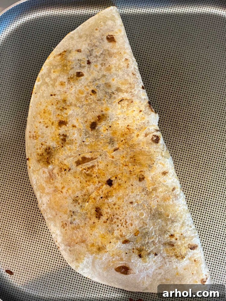 Folded steak quesadilla cooking on a hot griddle pan, achieving a perfect golden crisp