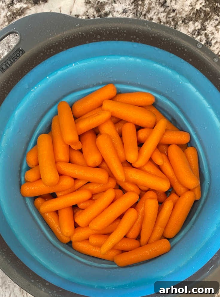 Raw baby carrots being rinsed in a colander under cold water.