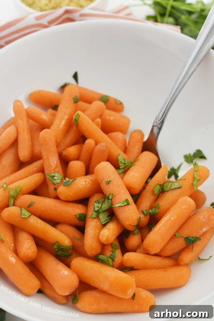 Cooked carrots with melted butter and brown sugar glaze, garnished with parsley in a white serving bowl.