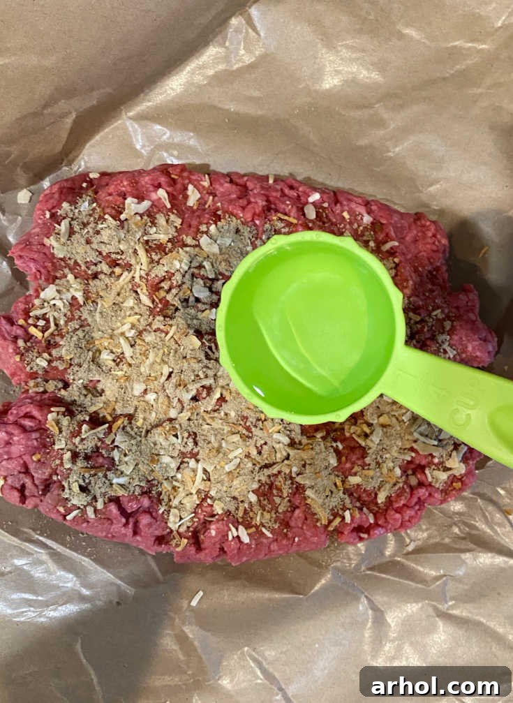 Close-up of seasoned ground beef mixed with Lipton onion soup mix and water in a large bowl, ready for patty formation.