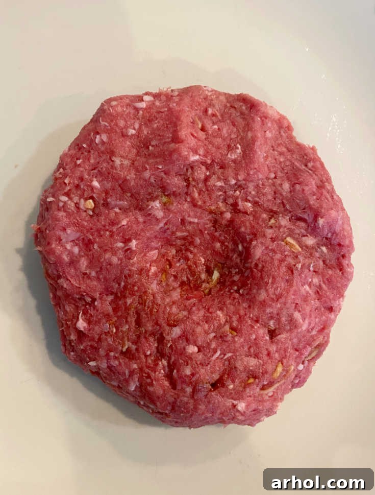 Raw hamburger patty with a thumb indentation in the center, demonstrating a technique to prevent shrinking during cooking.