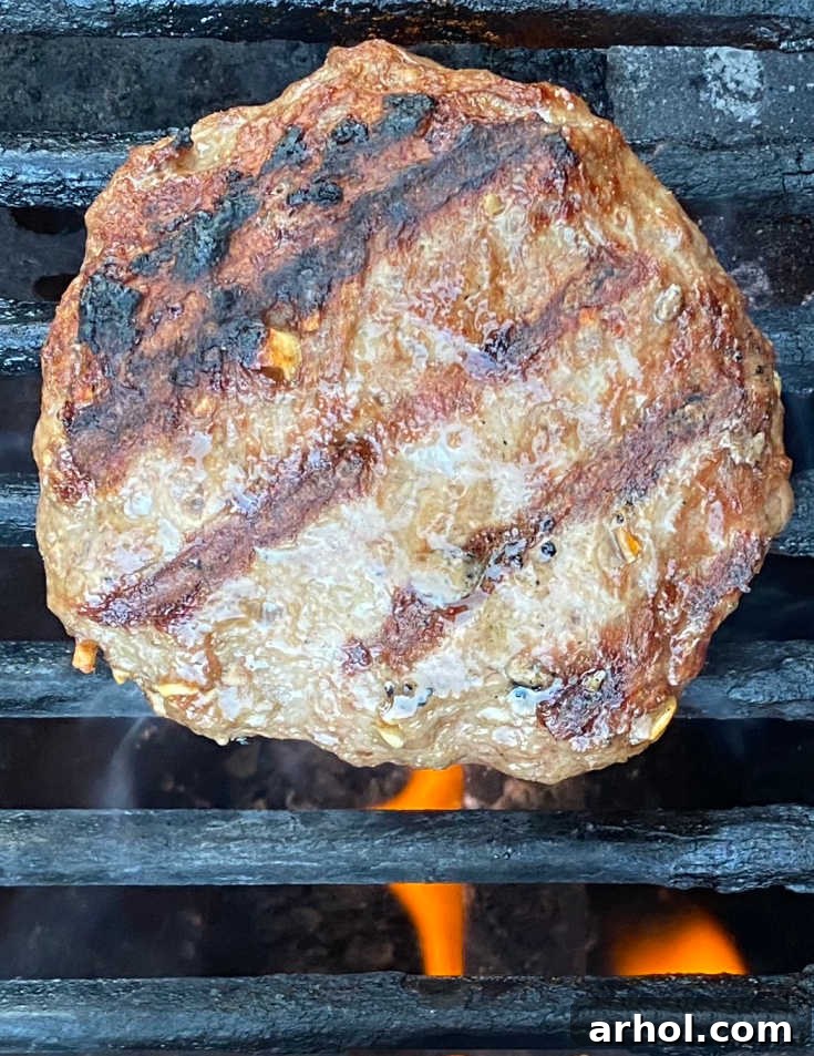 A delicious Lipton onion soup hamburger patty sizzling on a gas grill, with grill marks forming, signifying perfect cooking.