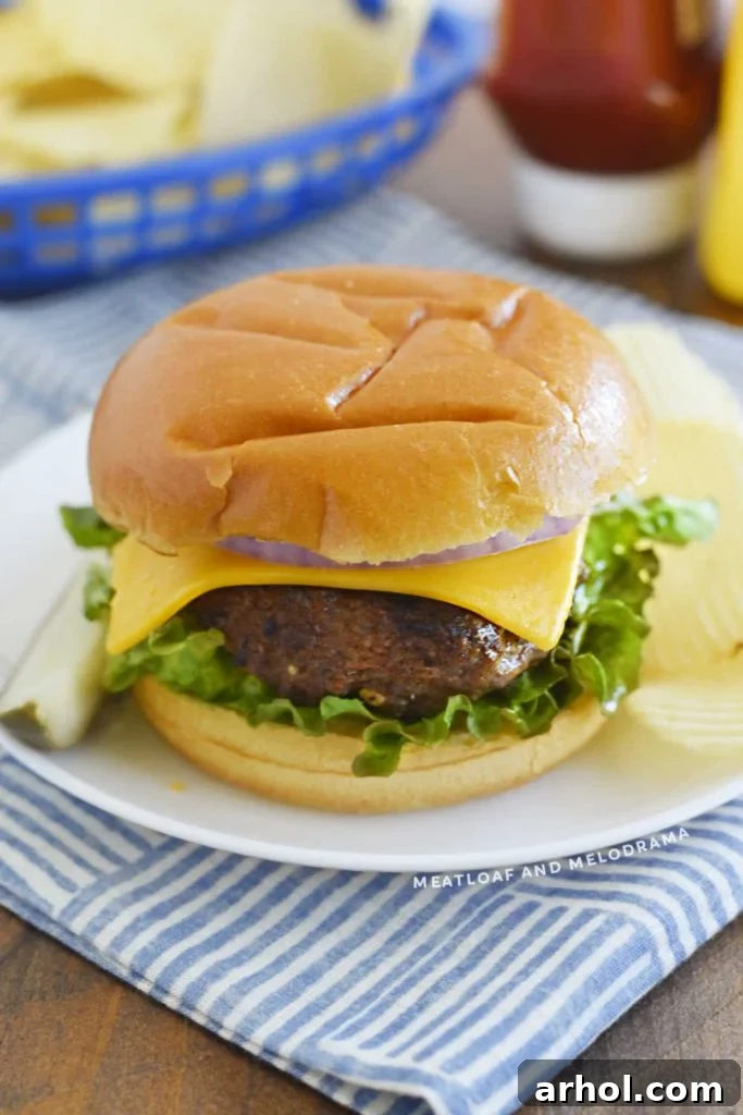 A perfectly cooked Lipton onion soup cheeseburger topped with crisp lettuce and red onion, served on a white plate in a toasted bun.
