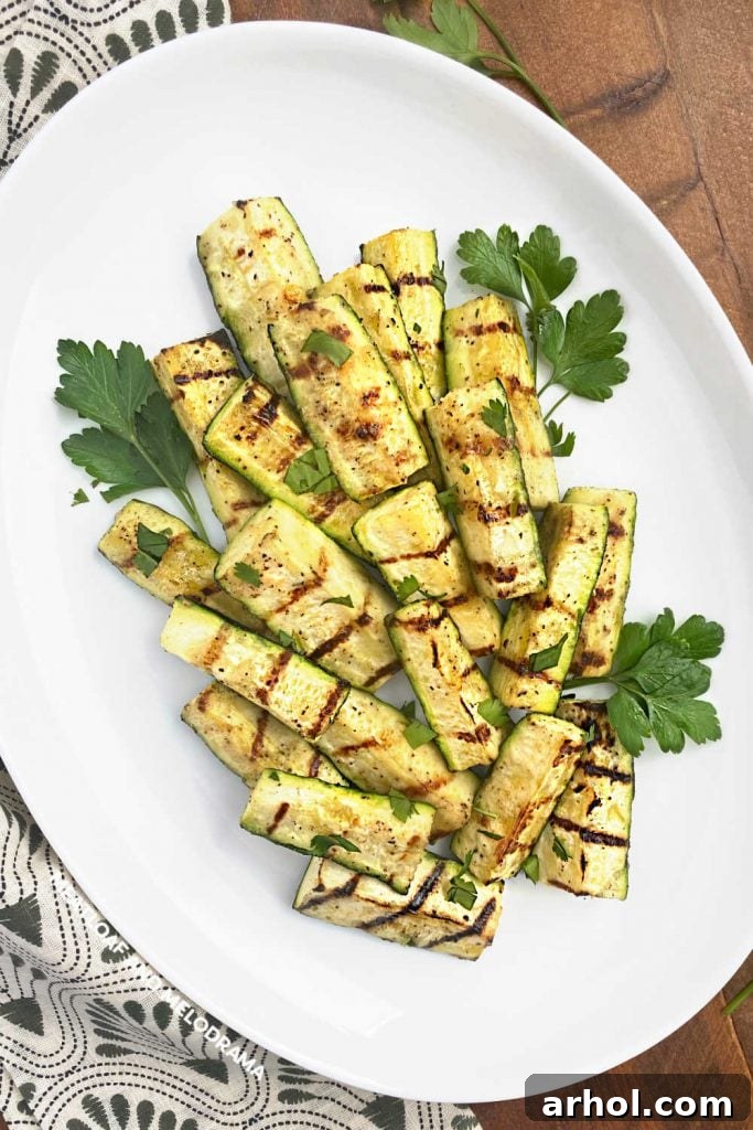 Grilled zucchini spears garnished with fresh parsley on a white platter, showcasing beautiful grill marks.