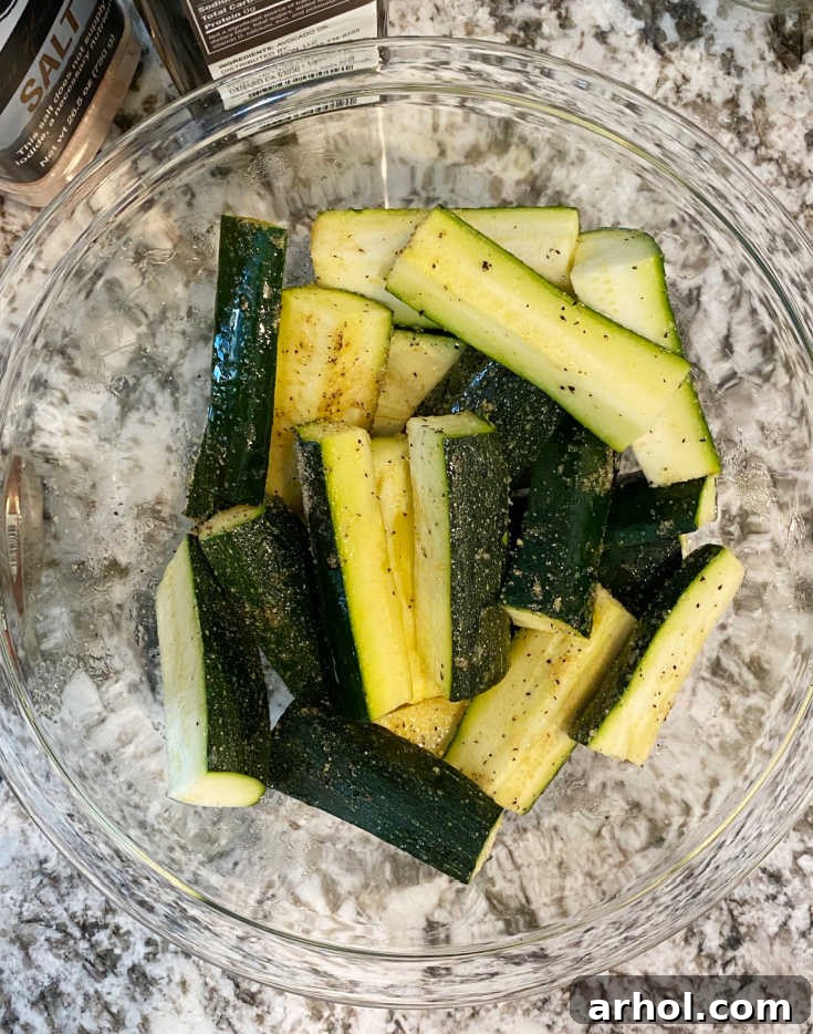 Zucchini spears coated with oil and seasonings in a mixing bowl.