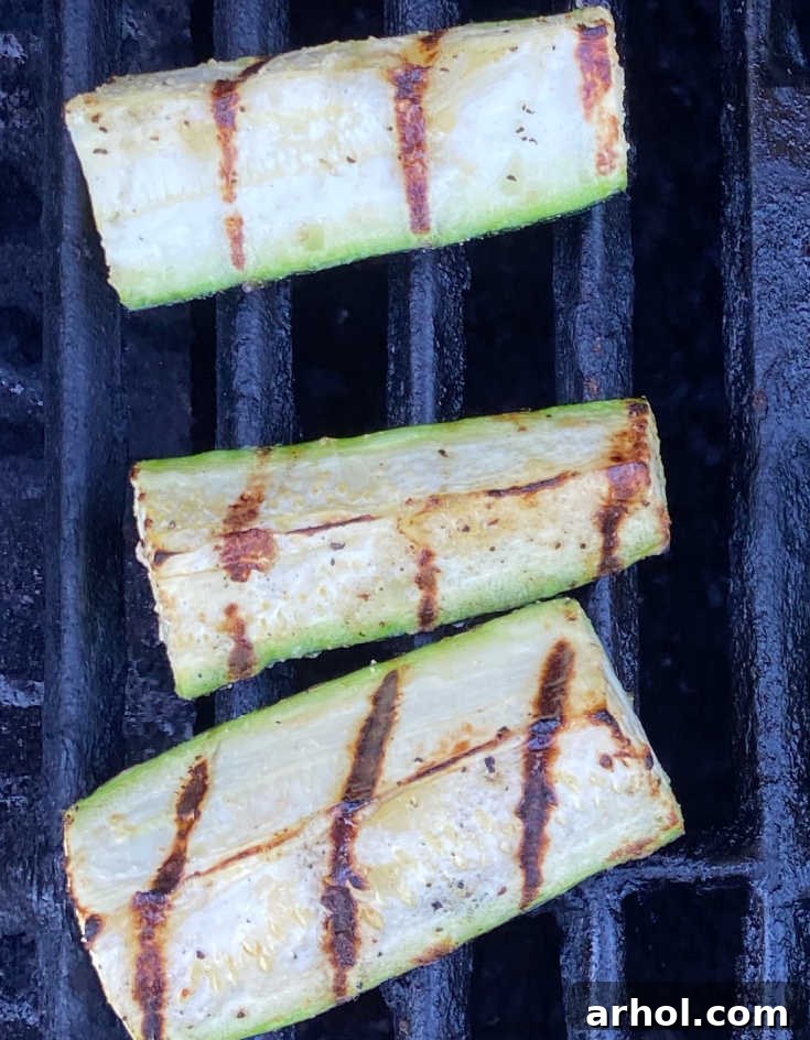 Zucchini spears cooking on a hot grill, showing developing grill marks.