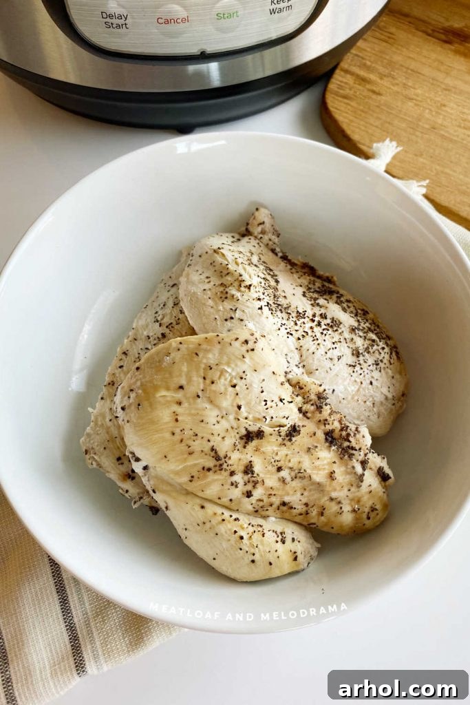 Two cooked chicken breasts in a white bowl, ready to be shredded or served, with an Instant Pot in the background.