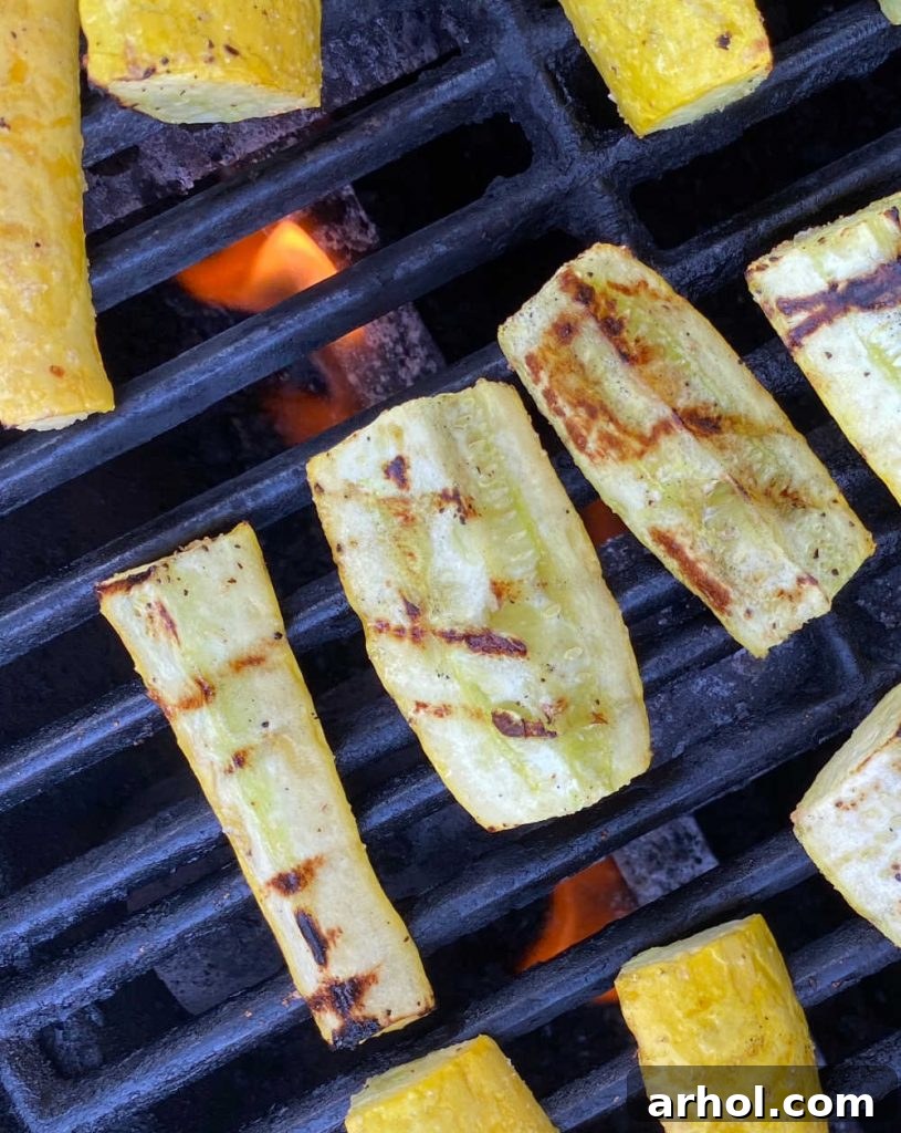 Sliced yellow summer squash cooking directly on the grates of a gas grill, showing developing char marks.