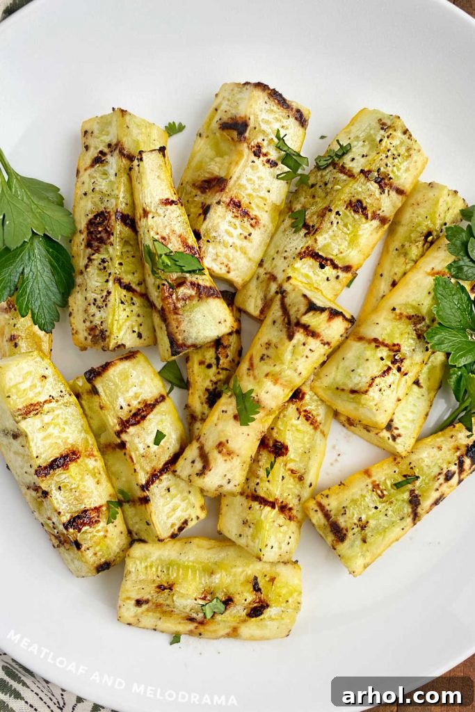 A close-up view of perfectly grilled summer squash, showing beautiful char marks and tender texture, served on a white platter.