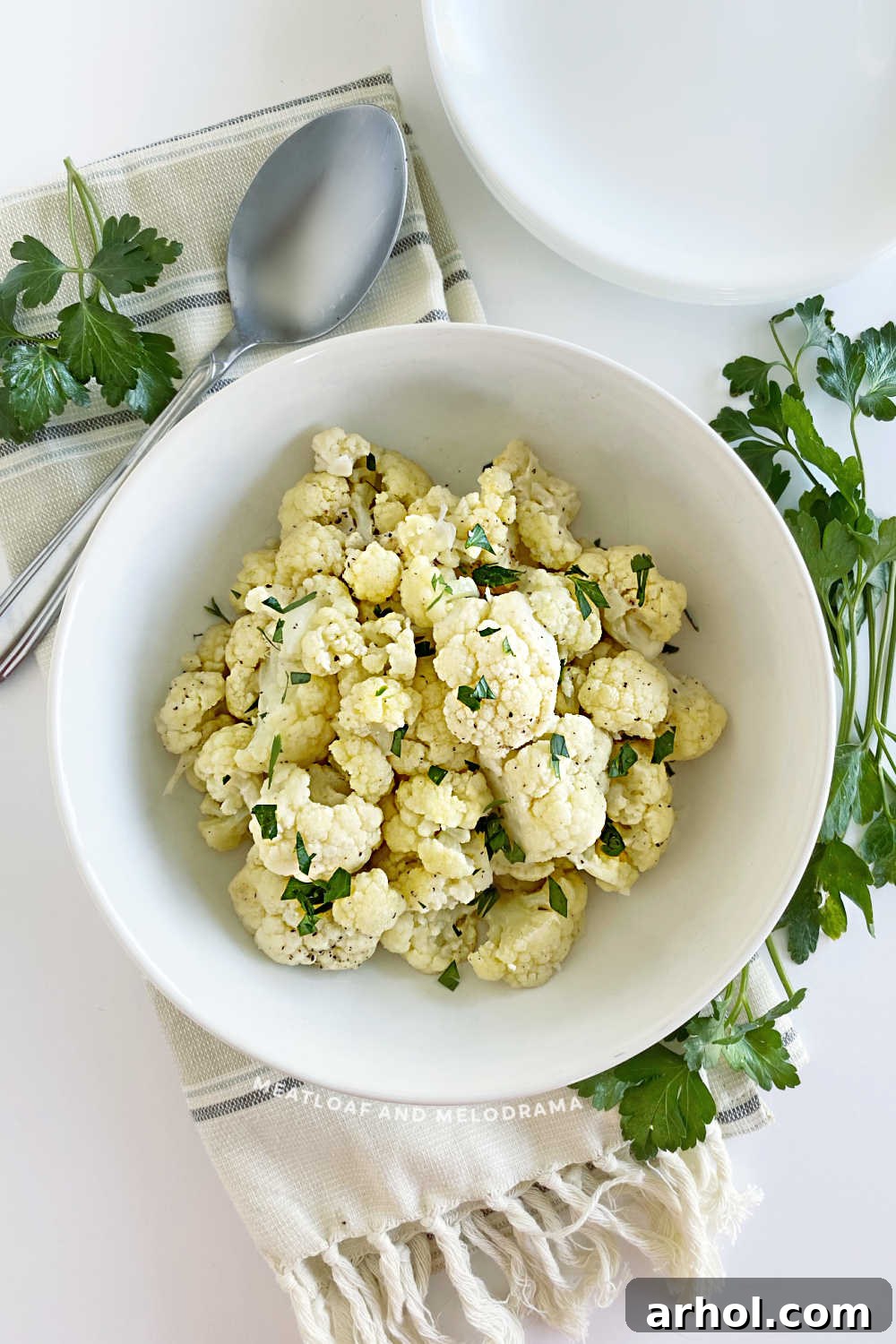 Steamed cauliflower garnished with fresh parsley in a white serving bowl.