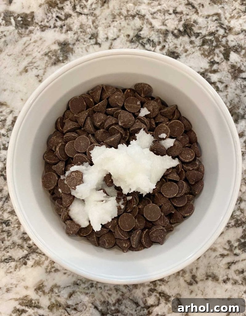 A white bowl filled with semi-sweet chocolate chips and a dollop of solid coconut oil, prepared for melting to create the chocolate coating.