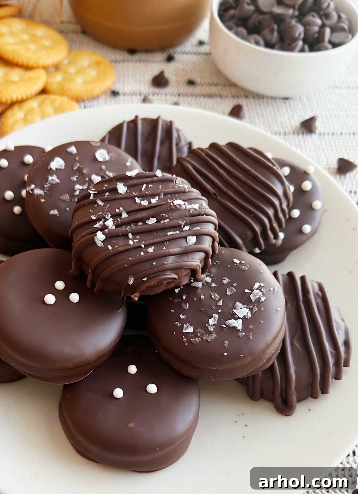 A visually appealing display of chocolate peanut butter Ritz cracker cookies on a white plate, some elegantly topped with flaky sea salt, while others are playfully decorated with colorful sprinkles, highlighting their versatility and deliciousness.