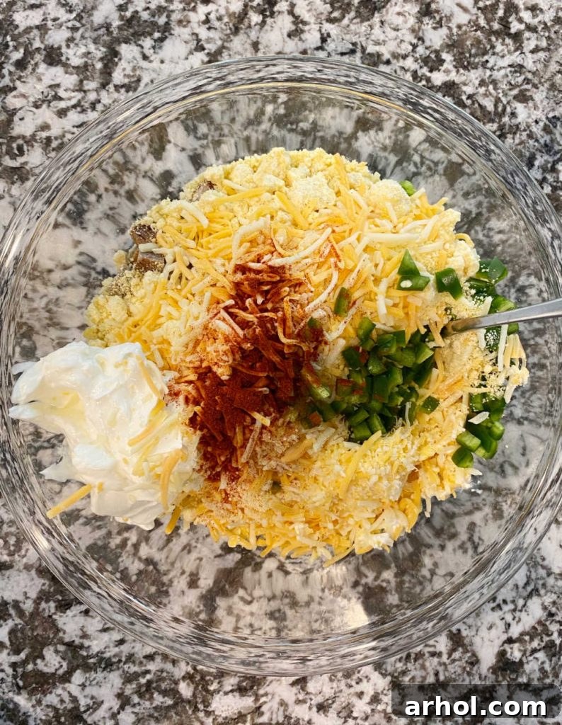A large mixing bowl filled with Jiffy muffin mix, shredded cheddar cheese, chopped jalapeño peppers, sour cream, and sausage, ready to be gently combined into a delicious batter.