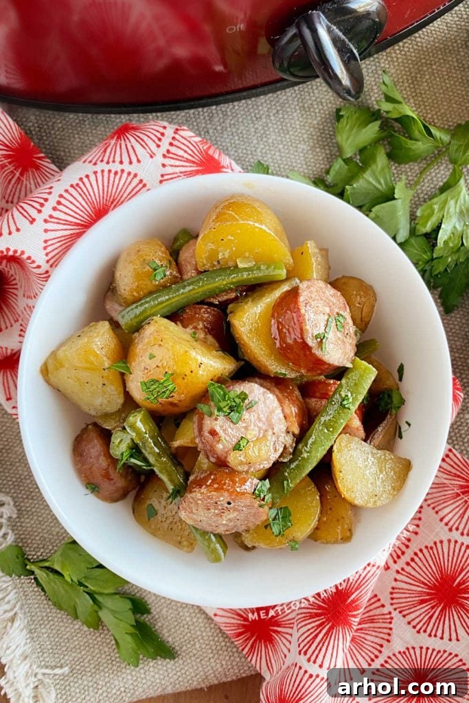 A serving of slow cooker sausage and potatoes with green beans in a white bowl, ready to eat.